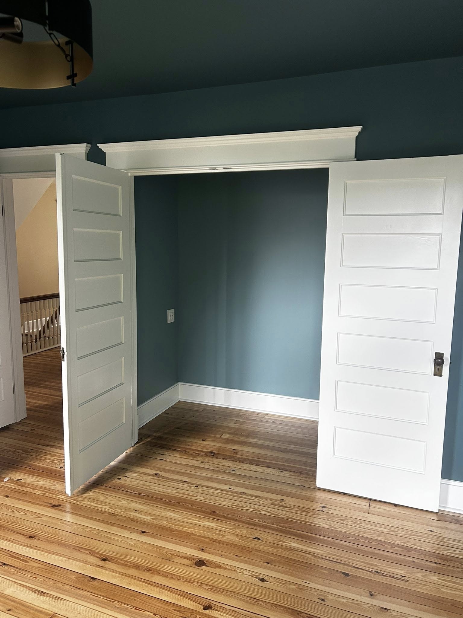 Bedroom with deep teal walls, white doors, and refinished hardwood floors